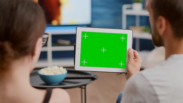Primo piano delle coppie che tengono tablet digitale con schermo verde guardando webinar e parlando