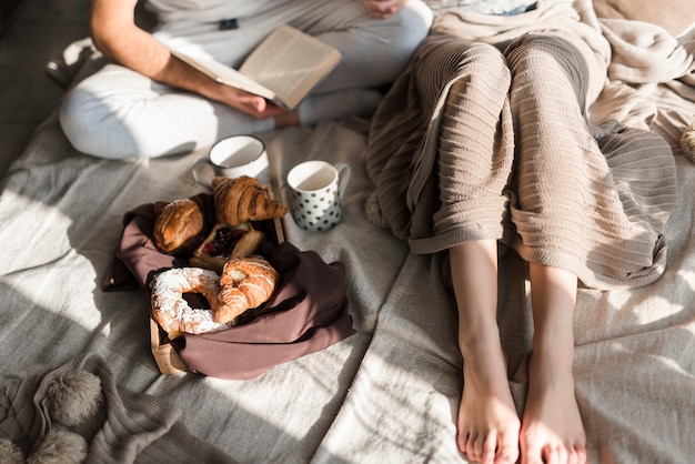 Primo piano delle coppie con il croissant e la tazza di caffè al forno sul letto