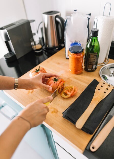 Primo piano delle fette di pomodoro di taglio a mano dell&#39;uomo sul bancone della cucina