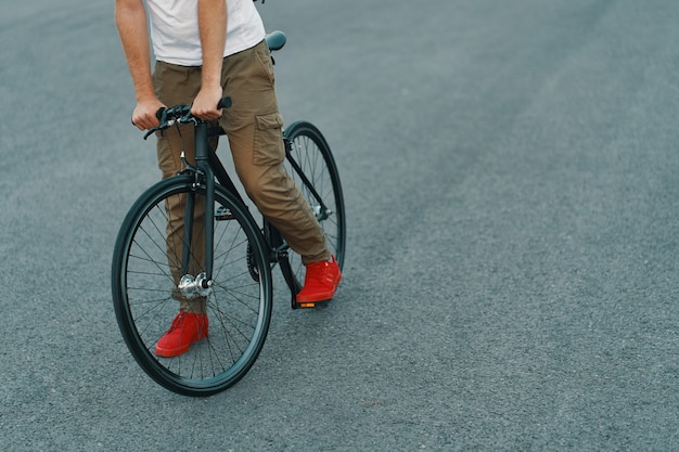 Primo piano delle gambe casuali dell'uomo che guidano bici classica sulla strada di città