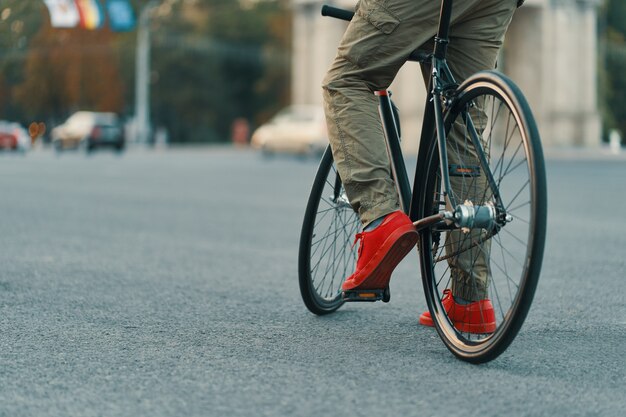 Primo piano delle gambe casuali dell'uomo che guidano bici classica sulla strada di città