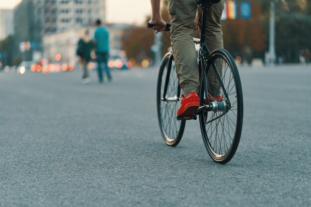 Primo piano delle gambe casuali dell'uomo che guidano bici classica sulla strada di città