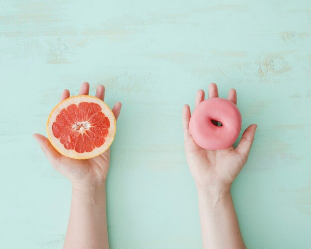 Primo piano delle mani che tengono la fetta di pompelmo e ciambella rosa sopra lo sfondo con texture