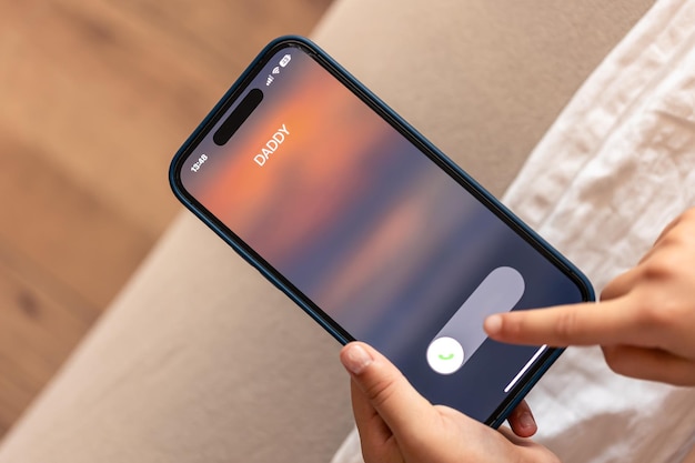 Primo piano delle mani del bambino che tengono il telefono con la chiamata in arrivo del papà sul display