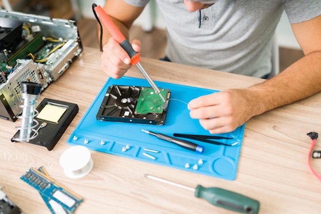 Primo piano delle mani del tecnico stagno di saldatura per saldare e riparare un disco rigido su una CPU rotta del computer