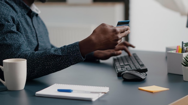 Primo piano delle mani dell'uomo afroamericano che digitano le informazioni della carta di credito sulla tastiera del computer, tempo di attività per lo shopping online in Internet. Pagamento aziendale con tecnologia web. Acquisto di operazioni di acquisto