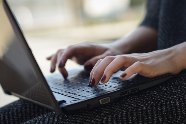 Primo piano delle mani della donna con le unghie dipinte digitando sul computer portatile