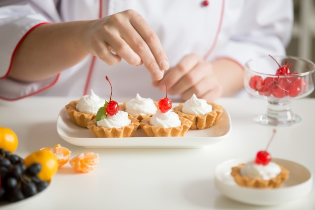 Primo piano delle mani femminili del confettero che sovrastano le torte della crema pasticcera