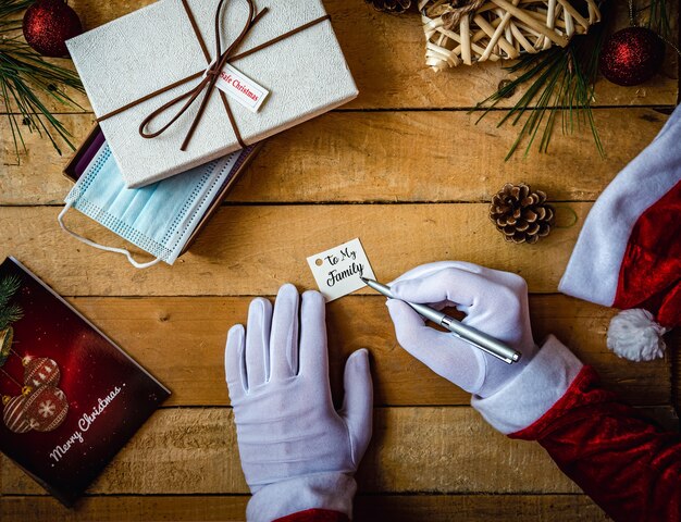 Primo piano delle mani in guanti bianchi che scrivono "Alla mia famiglia" su un biglietto per un regalo e una maschera