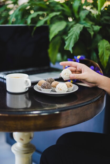 Primo piano delle palle di cioccolato mano di una persona con caffè e laptop sul tavolo di legno rotondo