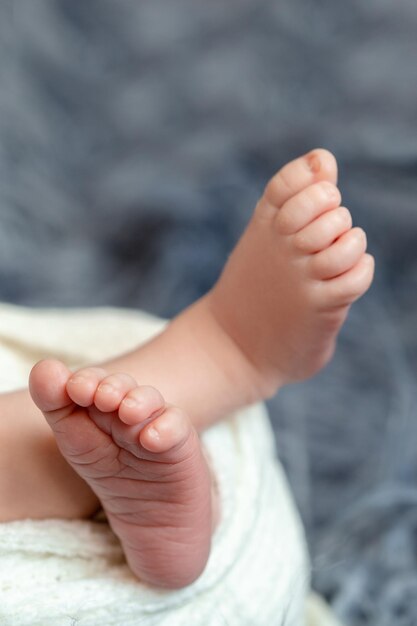 Primo piano delle piccole gambe del bambino. Il neonato addormentato sotto una coperta bianca lavorata a maglia giace sulla pelliccia blu. Neonato. 14 giorni.