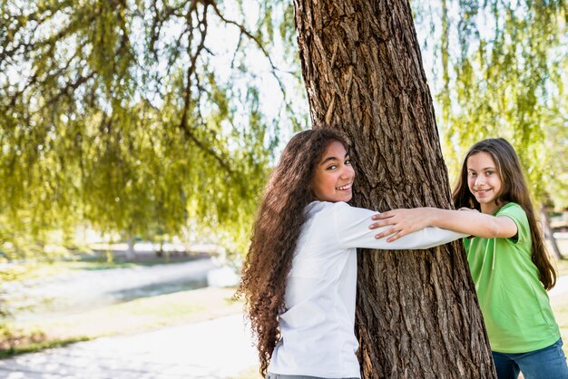 Primo piano delle ragazze sorridenti che si tengono mano che abbraccia grande albero nel parco