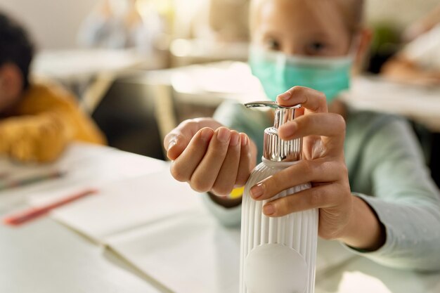 Primo piano dello studente elementare che disinfetta le mani in classe