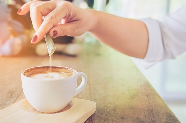 Primo piano dello zucchero di versamento della signora mentre preparando la tazza di caffè calda