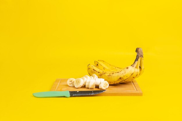 Primo piano di banane mature su un tagliere con un coltello isolato su uno sfondo giallo