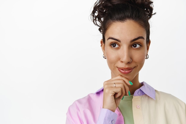 Primo piano di bella donna bruna con capelli pettinati, pelle del viso pulita, guardando premuroso al logo, promo sullo spazio vuoto sinistro, sfondo studio isolato.