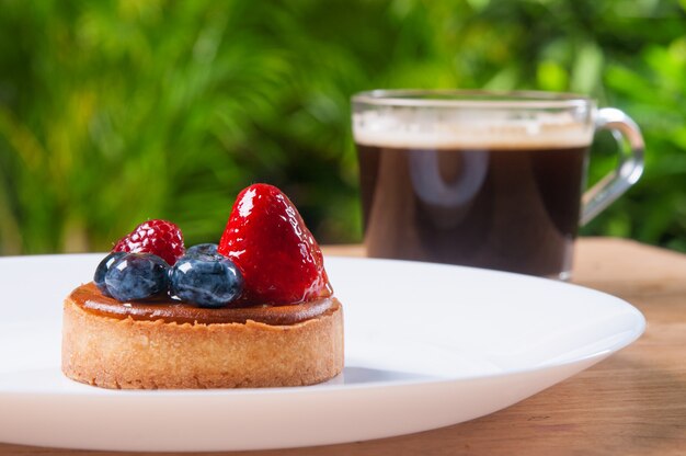 Primo piano di bella mini torta con le bacche e la tazza di caffè