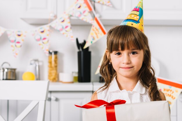 Primo piano di bella ragazza sorridente di compleanno che tiene il contenitore di regalo nella cucina
