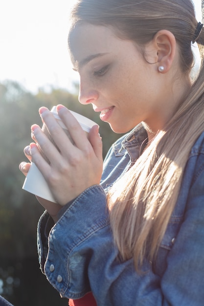 Primo piano di donna con una coda di cavallo e un caffè