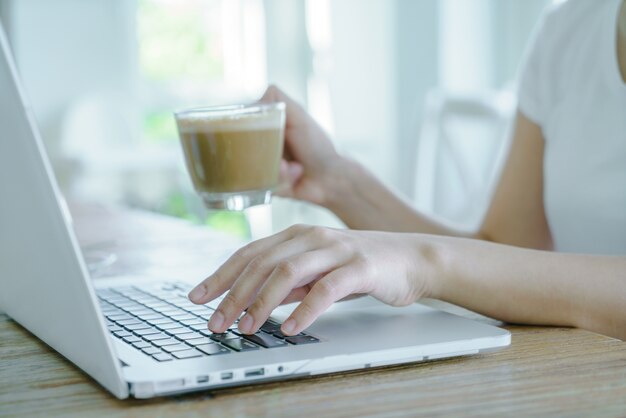 Primo piano di donna d&#39;affari mano digitando sulla tastiera del computer portatile e cof