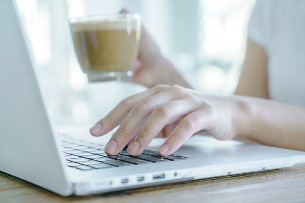 Primo piano di donna d&#39;affari mano digitando sulla tastiera del computer portatile e cof