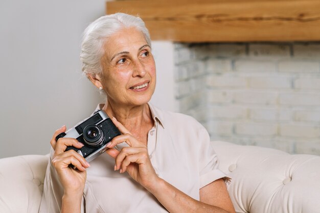 Primo piano di donna senior tenendo in mano la fotocamera in cerca di distanza