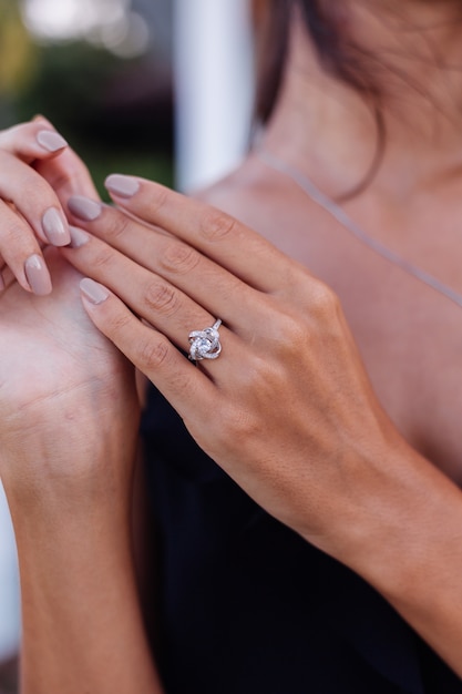 Primo piano di elegante anello di diamanti sul dito della donna. Donna che indossa un abito nero. Concetto di amore e matrimonio. Luce diurna naturale morbida e messa a fuoco selettiva.