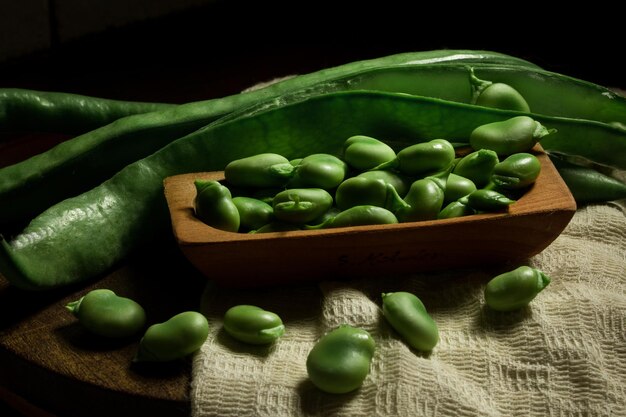 Primo piano di fave crude fresche nei baccelli e un mucchio di fagioli nel piatto di legno