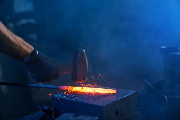 Primo piano di forti mani maschili che forgiano metallo fuso sull'incudine