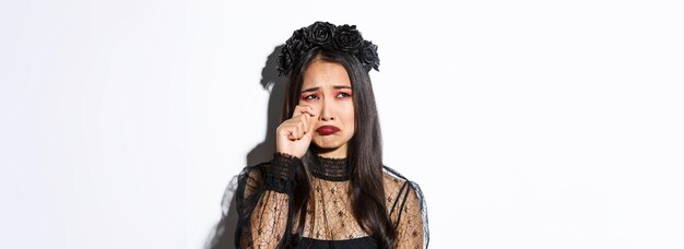 Primo piano di giovane donna asiatica in costume da strega che piange e sembra triste sentirsi triste in piedi sopra