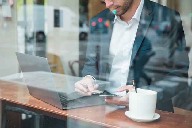 Primo piano di giovane uomo d&#39;affari che utilizza la carta di credito sul telefono cellulare nel caffè