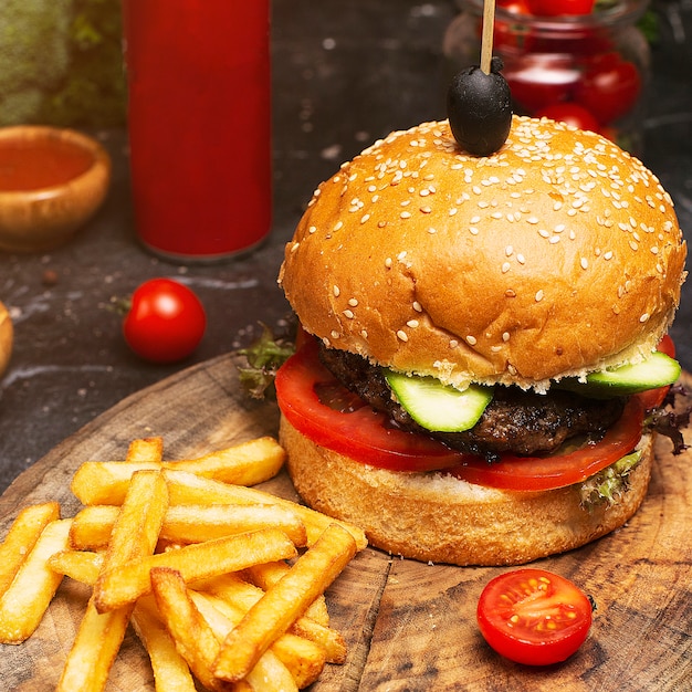 Primo piano di hamburger fatto in casa con carne di manzo, pomodoro, lattuga, formaggio e patatine fritte sul tagliere. Fast food