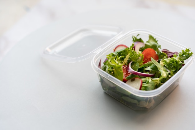 Primo piano di insalata fresca in una scatola di plastica su una superficie bianca