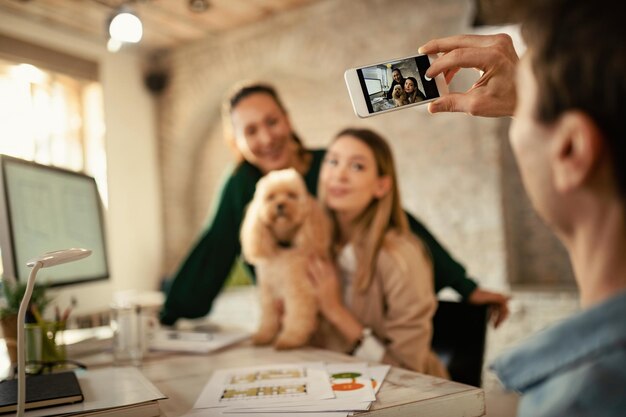 Primo piano di lavoratori freelance e il loro cane fotografati con lo smartphone in ufficio