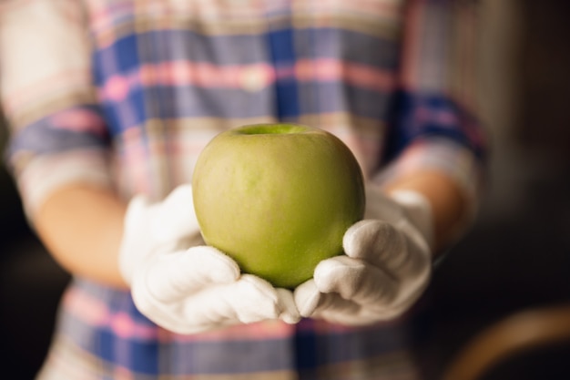 Primo piano di mani femminili in guanti che tengono mela verde, cibo sano, frutta. Dieta nutrizione biologica, prodotto naturale e fresco ricco di vitamine. Preparare, proporre per qualcuno. Copyspace.