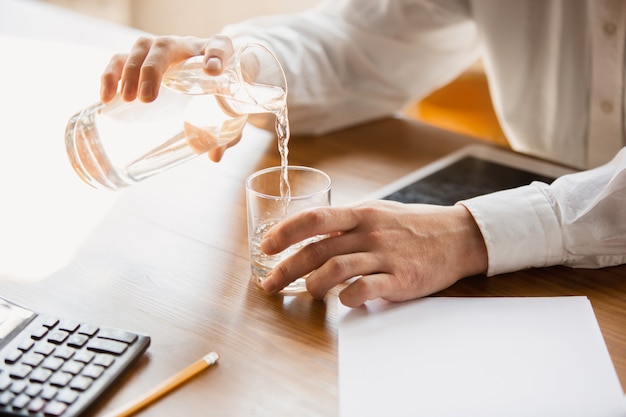 Primo piano di mani maschili caucasiche che versano acqua in un bicchiere. Concetto di affari, finanza, lavoro, acquisti online o vendite.