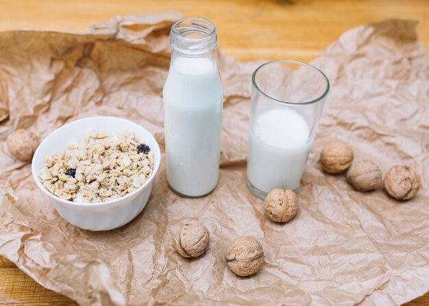 Primo piano di noci; latte e ciotola di cereali su carta marrone sbriciolata