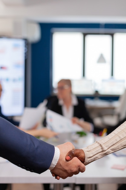 Primo piano di partner commerciali multirazziali in piedi di fronte al desk della conferenza che si stringono la mano dopo aver firmato il contratto di partnership