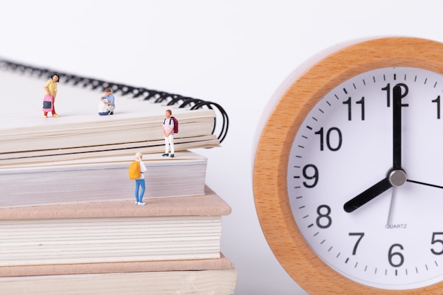 Primo piano di piccole figurine di studenti in piedi sui libri di testo accanto a un orologio