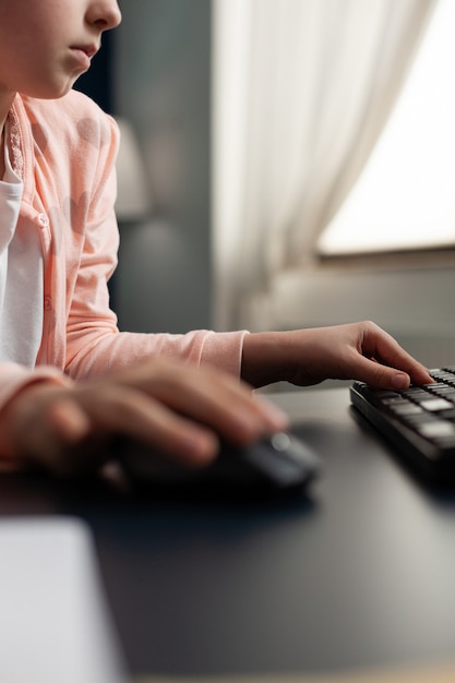 Primo piano di piccole mani di scolaro che usano il computer per l'istruzione a distanza