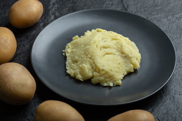 Primo piano di purè di patate su un piatto e patate fresche intorno.