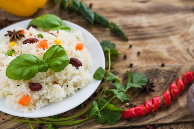 Primo piano di riso sano; foglie di basilico; sul piatto con prezzemolo e peperoncino su sfondo sfocato