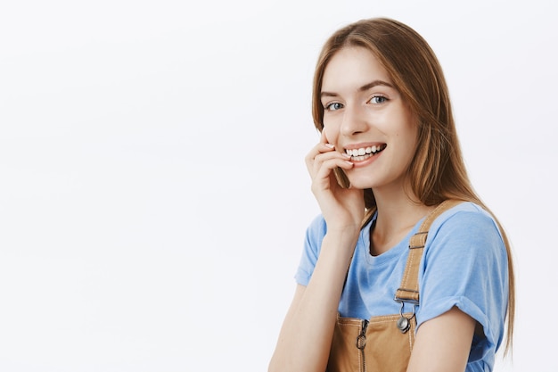 Primo piano di sognante bella ragazza sorridente, toccando il viso delicatamente e guardando civettuolo