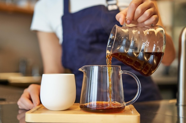 Primo piano di un barattolo di vetro e una tazza in piedi sul bancone del bar barista versando il caffè filtrato e preparando