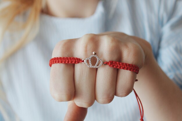 Primo piano di un braccialetto di filo rosso con un ciondolo a corona d'argento sulla mano di una donna