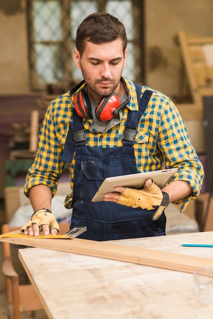 Primo piano di un carpentiere maschio che esamina compressa digitale che misura il blocco di legno