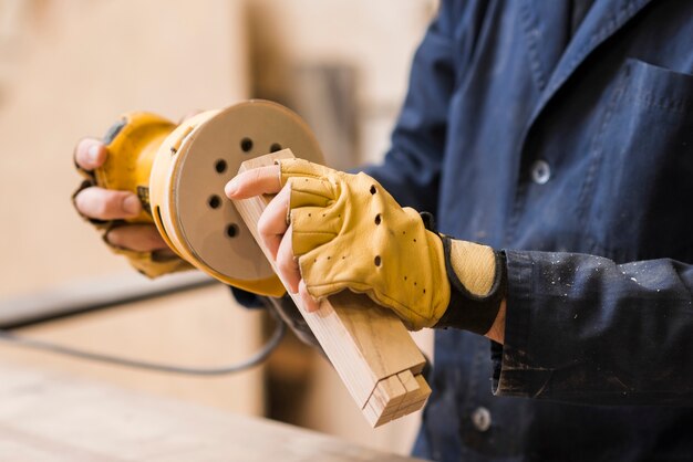 Primo piano di un carpentiere maschio che insabbia un blocco di legno con la sabbiatrice