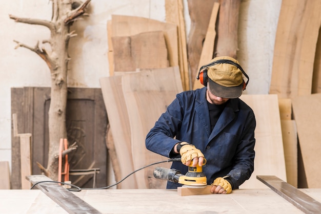 Primo piano di un carpentiere maschio che usando sabbiatrice elettrica su legno