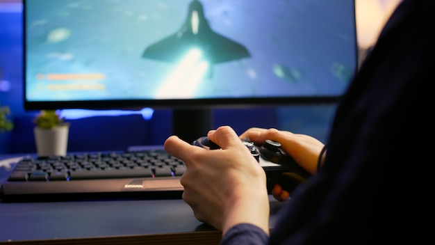 Primo piano di un cyber gamer professionista che gioca a un videogioco sparatutto spaziale utilizzando un controller wireless