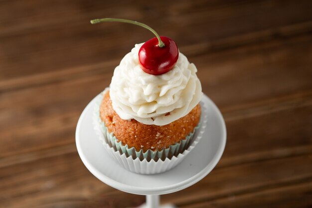 Primo piano di un delizioso cupcake con crema e ciliegia in cima su un supporto da dessert